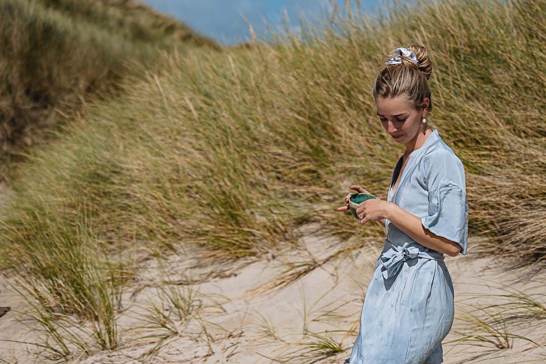 Kvinde i klitterne iført en lyseblå plantefarvet silkekimono og en håndfarvet scrunchie i håret